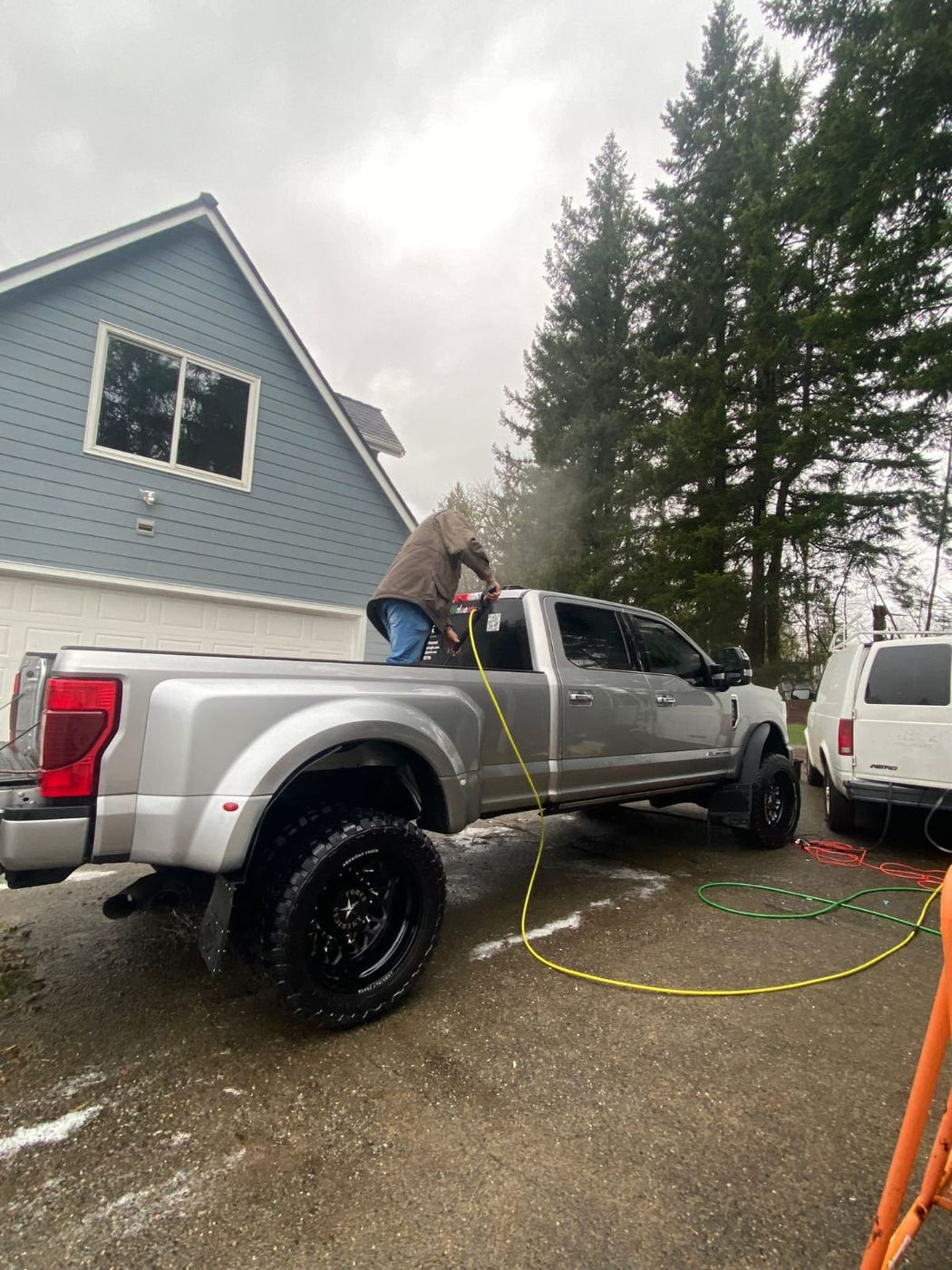Pressure-washing a lifted silver pickup in a driveway
